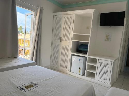 ein weißes Schlafzimmer mit Bett und Fernseher in der Unterkunft Jequitiba Hotel Frente ao Mar in Guarujá