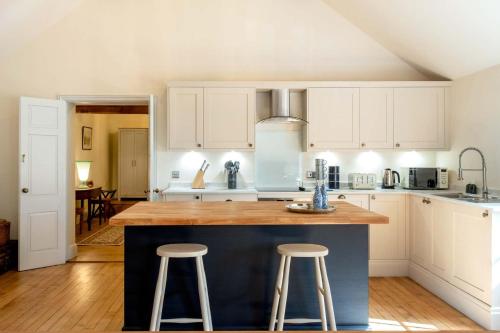 a kitchen with white cabinets and a blue island with stools at The Coach House in Barlestone