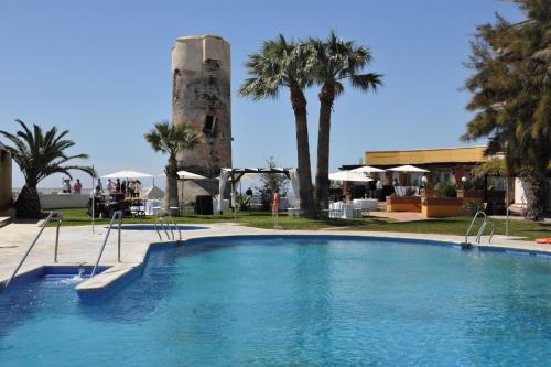 a swimming pool in front of a building with a tower at Hotel Salobreña Suites in Salobreña