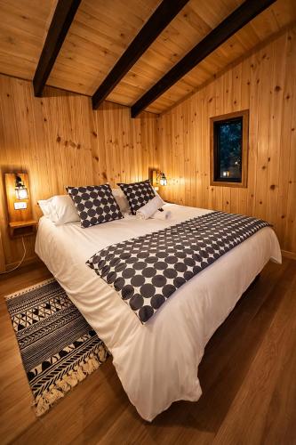 a large bed in a room with wooden walls at Cabaña Alto del Bosque in Coñaripe