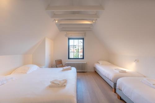 two beds in a room with white walls and a window at Calm, Light-Filled Apartment with Private Balcony in Knokke-Heist