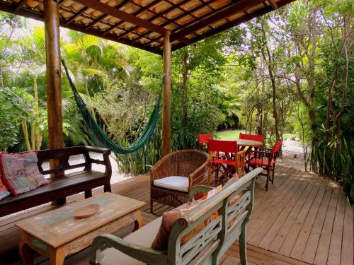 a porch with chairs and tables and a hammock at Casa Morada dos Pássaros - 3 suítes in Imbassai