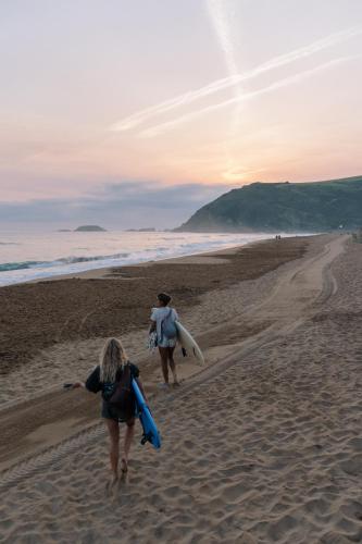 two people walking on the beach with surfboards at San Sebastian Surf and Party Hostel in Aia