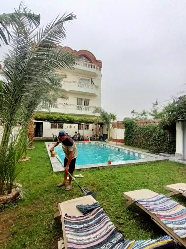 a man is mowing the grass next to a swimming pool at Villa Set ma'at Nile view in Luxor