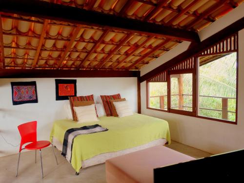 a bedroom with a bed and a red chair at Casa Morada dos Pássaros - 3 suítes in Imbassai