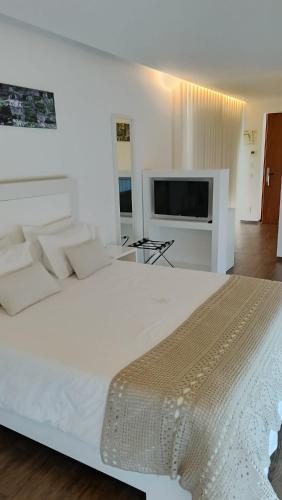 a white bedroom with a large bed and a flat screen tv at CANTINHO D'AVÓ - Apúlia in Areia