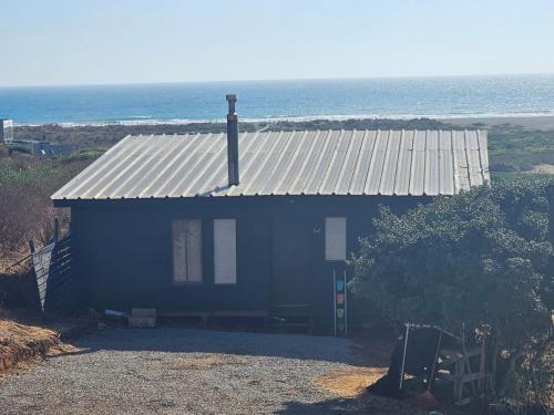 a blue house with a tin roof and the ocean at Aegla lodge in Pichilemu