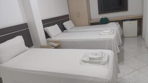 a room with three beds and a tv in it at Hotel Minas Brasil in Montes Claros
