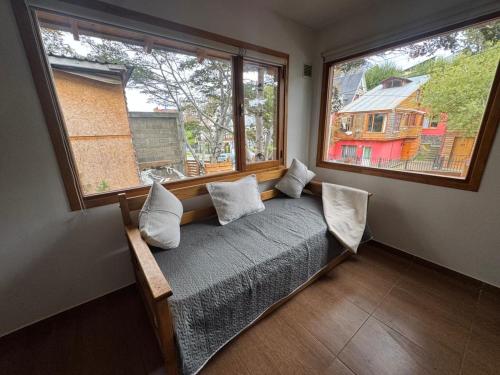 a bed in a room with two large windows at Las raíces departamentos in Ushuaia