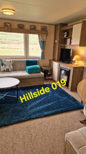 a living room with a couch and a blue rug at Lyons Sunnysands - Hillside 019 in Barmouth