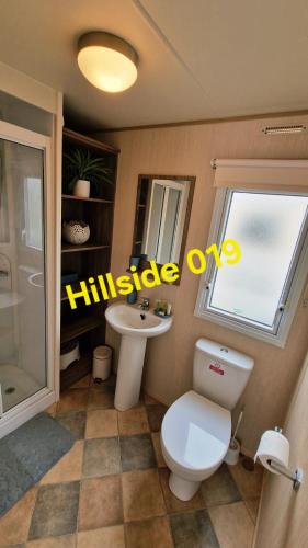 a bathroom with a toilet and a sink and a window at Lyons Sunnysands - Hillside 019 in Barmouth