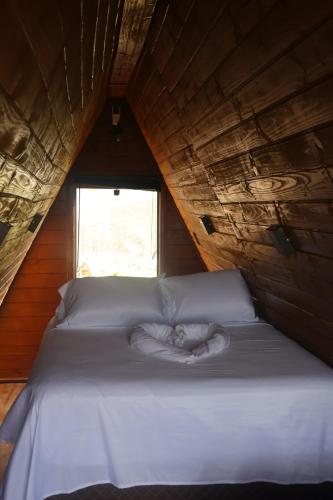 a white bed in a wooden room with a window at Cabana Janela do Céu in Jaboticatubas