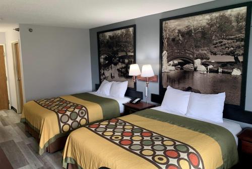two beds in a hotel room with paintings on the wall at Super 8 by Wyndham Chenoa in Chenoa
