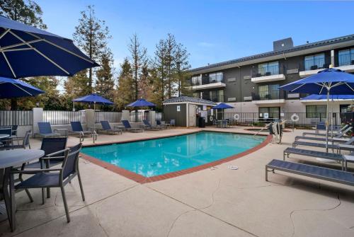 a swimming pool with chairs and blue umbrellas at Howard Johnson by Wyndham Fullerton/Anaheim Conference Cntr in Fullerton