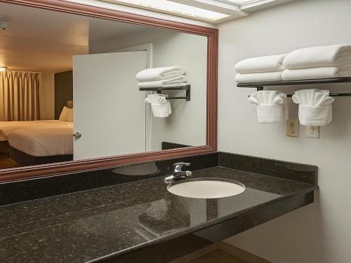 a bathroom with a sink and a mirror and a bed at Rancho San Diego Inn & Suites in El Cajon