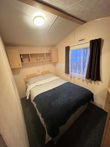 a small bedroom with a bed and a window at Seawick Beach Caravan in Saint Osyth