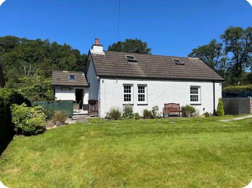 a white house with a bench in a yard at Stunning country home with private wellness Spa in Strachur