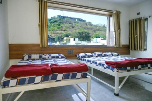 two beds in a room with a large window at Laxman AC Lodge Jejuri - by Martandbhairav hospitality LLP in Jejūri