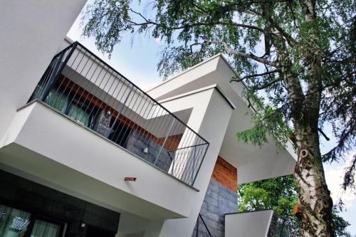 a white house with a balcony next to a tree at Villas and apartments Oaza in Sarajevo