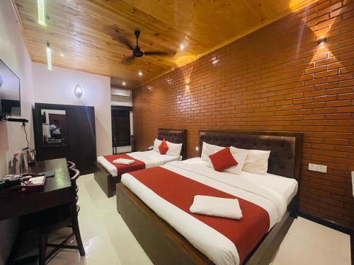 a bedroom with two beds and a desk and a brick wall at J Hotel in Jaffna