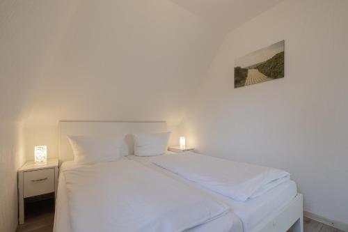 a white bed in a bedroom with a picture on the wall at Meeresbrandung in Süderende