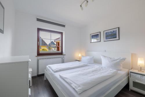a white bedroom with a bed and a window at Robbennest in Süderende