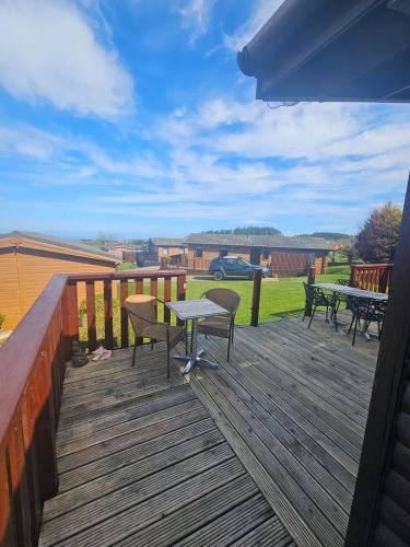 a wooden deck with tables and chairs on it at 3-Bed Ocean View Lodge - Parking & Terrace in Ilfracombe