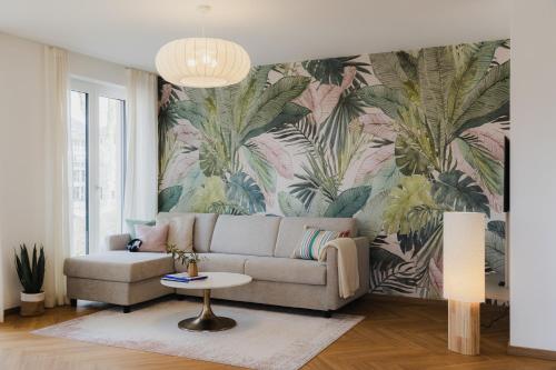 a living room with a couch and a tropical wallpaper at LÆKE Apartments - Lindau am Bodensee in Lindau