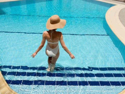 Eine Frau mit Hut, die in einem Schwimmbecken spaziert in der Unterkunft Mövenpick Hotel Doha in Doha