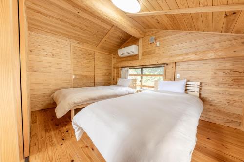 zwei Betten in einem Zimmer mit Holzwänden in der Unterkunft Amakusa LogHouse UmiOTO 海音 in Amakusa