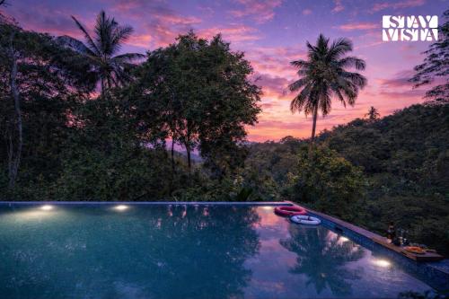 a swimming pool in front of a forest with a sunset at StayVista at Aradhya Villa with Infinity Pool, Lawn in Wayanad
