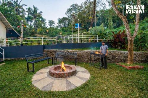 a man standing next to a fire pit in a yard at StayVista at Aradhya Villa with Infinity Pool, Lawn in Wayanad