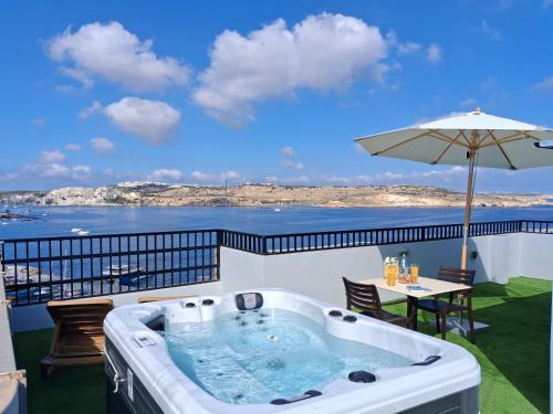 a hot tub on a balcony with a table and an umbrella at Islet Promenade Studio with Hot Tub and Panoramic Sea Views by GetawaysMalta in St. Paul's Bay