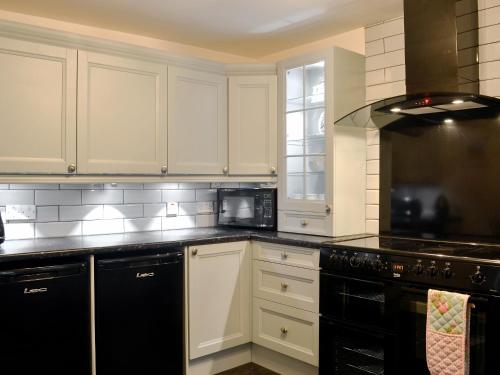 a kitchen with white cabinets and black appliances at Raglan Cottage in Ardentinny