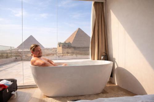 a man in a bath tub in a room with pyramids at LE Grand Pyramids View & Suites in Cairo