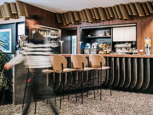 a man is walking past a bar with chairs at Mercure Brest Centre Port in Brest