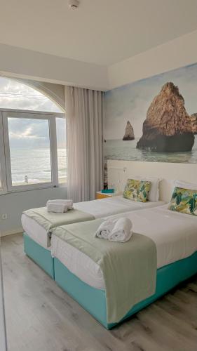 two beds in a bedroom with a view of the ocean at Golden Beach Guest House & Rooftop Bar in Faro