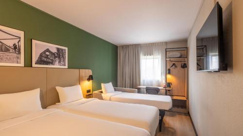 a hotel room with two beds and a chair at Campanile PRIME - Roissy - Aéroport Paris CDG in Roissy-en-France