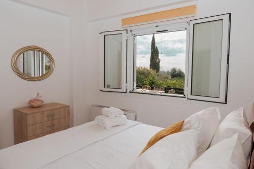 a white bedroom with a bed and a window at Nafos Villa Stella in Levkákia