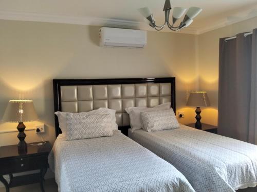 a bedroom with two beds with white sheets and lamps at Camdale Guesthouse in Cape Town
