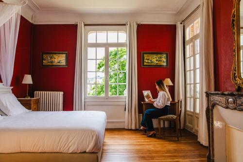 a woman sitting at a desk in a bedroom reading a book at La Villa L'Argentine in Cabourg