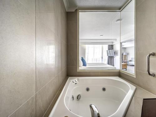a white bath tub in a bathroom with a mirror at Novotel Cairns Oasis Resort in Cairns