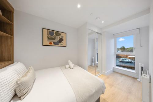 a white bedroom with a bed and a window at Modern & Cozy 2-Bedroom Apartment plus Parking, Gym, Cinema, Games Room, Workspace in New Malden