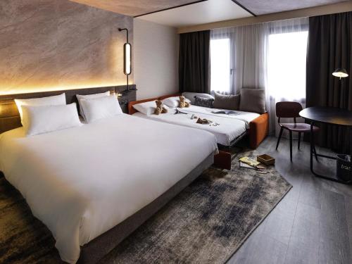 a hotel room with a large white bed and a desk at Novotel Paris Suresnes Longchamp in Suresnes