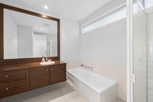 a bathroom with a tub and a sink and a mirror at Breakers Holiday House in Lorne