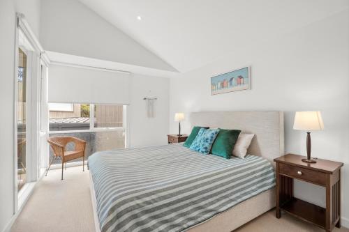a white bedroom with a bed and a window at Breakers Holiday House in Lorne