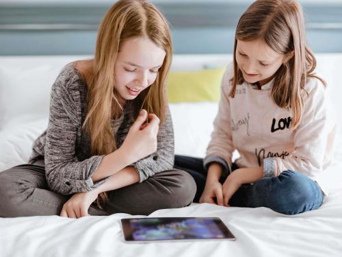 two girls sitting on a bed looking at a tablet at ibis Liverpool Centre Albert Dock – Liverpool One in Liverpool
