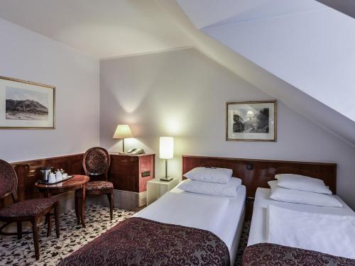 a hotel room with two beds and a table and chairs at Mercure Grand Hotel Biedermeier Wien in Vienna