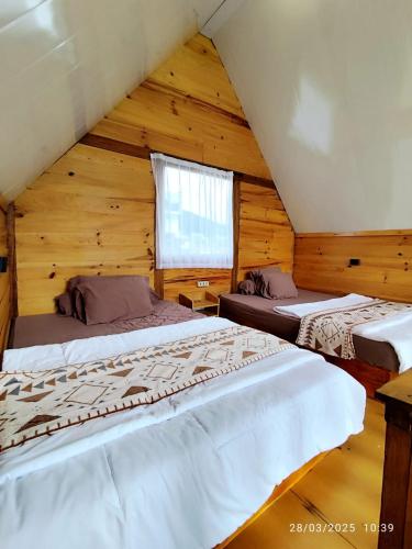 two beds in a log cabin with a window at Glamping Dieng New in Diyeng