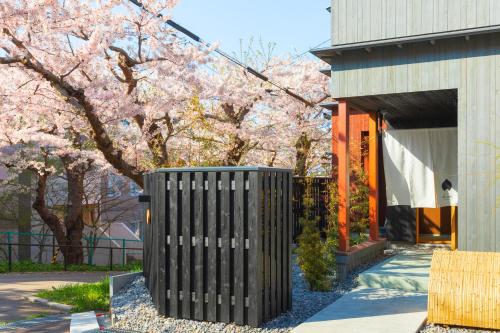 a black trash can in front of a building withakura trees at 住三吉の宿 桜山路 in Hakodate